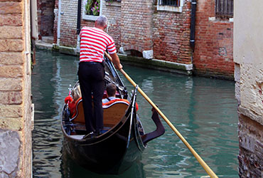 Gondolier aboard a gondola navigating along a canal in Venice