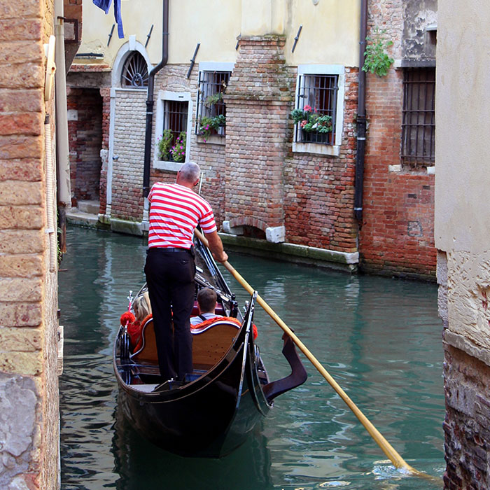 Gondolier aboard a gondola navigating along a canal in Venice